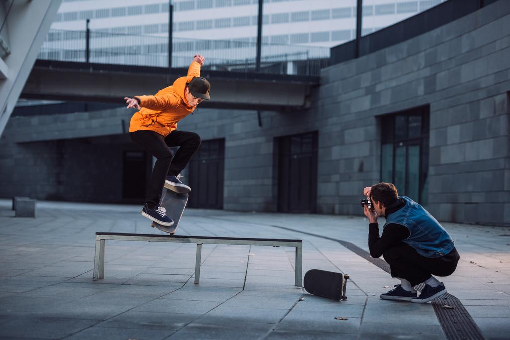 Man taking photo of skateboarder doing trick over bench